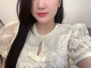 JuciPie poses in a white lace blouse with a pearl-trimmed collar, showing her long black hair and smiling face.