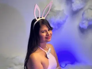 Smiling young woman in a white bunny ear headband and pink outfit posing in a dreamy blue cloud setting.