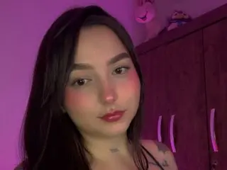 KAROLLMONROE poses with long dark hair and red lipstick against a purple background, showing her face and shoulders.