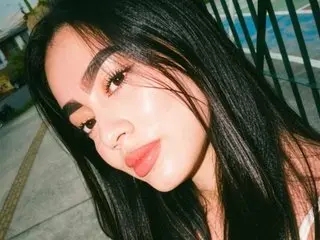 KIMBERLYRIOSS poses with long black hair and red lipstick, looking directly at the camera in a close-up shot.