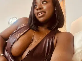 Smiling Black woman in a brown leather dress relaxing indoors with a warm, glowing mood.