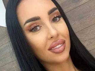 Woman with long dark hair and glamorous bronze makeup smiling in a bright indoor setting.