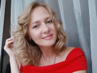Smiling blonde woman in a red off-the-shoulder top posing against a grey textured background.