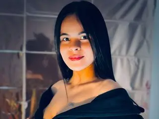 KandyMorgan69 poses with long black hair, wearing a black off-the-shoulder top against a soft, indoor background.
