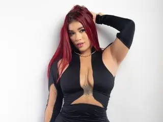 Confident woman with red hair in a black cutout dress posing against a white background.