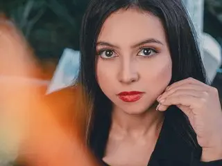 KassandraWood poses with long dark hair and red lipstick, looking directly at the camera in a close-up shot.