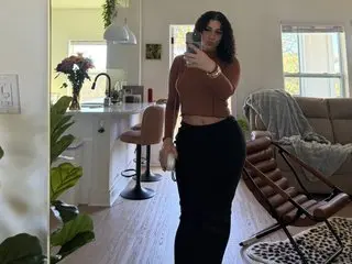 KatReeseXO poses in a brown long-sleeve top and black pants, holding a phone for a mirror selfie in a bright room.
