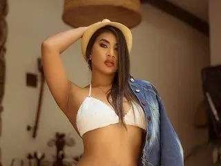 KataaLopez poses with one hand in her hair, wearing a white bikini top and a denim jacket over her shoulders.