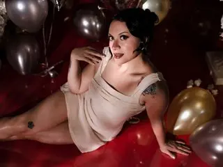 Glamorous woman in a white satin dress reclining among silver and gold balloons in a moody, festive setting.