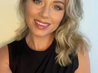 KateDivine69 smiles with her blonde wavy hair, wearing a black sleeveless top against a plain white background.