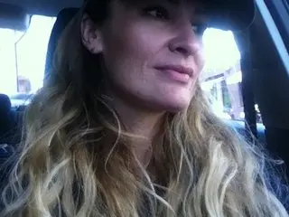 KatieSkyMadison — Smiling blonde woman in a black cap sitting in a car on a bright day.