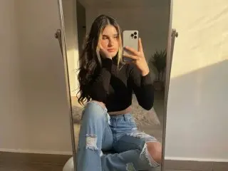 KatieVance takes a mirror selfie wearing a black long-sleeve crop top and ripped blue jeans while sitting on the floor.