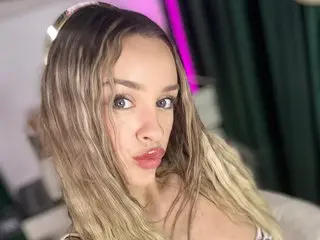 KatieeCutieXoo poses close-up, looking at the camera with her long blonde hair framing her face and her lips slightly parted.