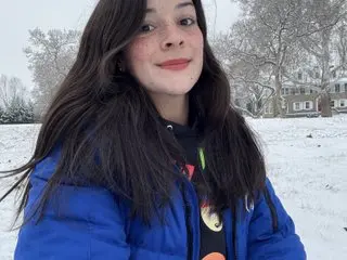 KatteSweett poses outdoors in a blue puffer jacket with her long dark hair down against a snowy winter background.