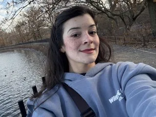 KatteSweett — KatteSweett smiles for a selfie in a blue hoodie while standing outdoors near a lake and trees.