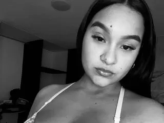 Kattymiller18 poses close-up, looking at the camera with her dark hair down and a small mole on her nose, showing her bare shoulders and chest.