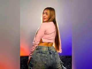 KatyBennet poses in a pink long-sleeve crop top and denim jeans, looking back over her shoulder.
