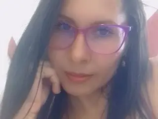 KeiryDiaz with long dark hair, wearing purple-tinted glasses and looking directly at the camera in a close-up headshot.