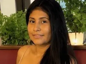 Kendra_Foox smiling at the camera with long dark hair in an indoor setting with green plants.
