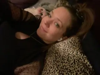 KennedyNova777 smiles while lying back, wearing a black top with her brown hair loose or pulled back slightly.