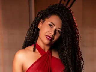 Elegant woman with long curly hair wearing a red halter dress in a warm, moody indoor setting.
