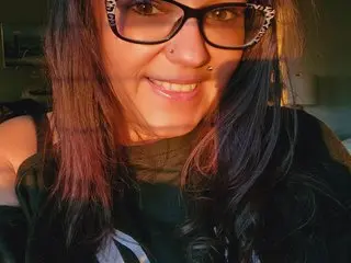 Smiling woman with dark hair and glasses wearing a black top in warm, cozy indoor lighting.
