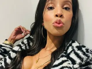 Keyler_True18 poses with long dark hair, wearing a black and white patterned jacket that shows cleavage, looking at the camera with a pouty lip.