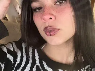 Kikivelvet shows her face and shoulders, wearing a black and white patterned top with her long dark hair down.