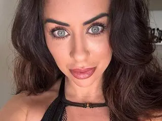 KimberleyJBabestation poses close-up with her long dark hair, blue eyes, and pink lipstick, wearing a black choker.