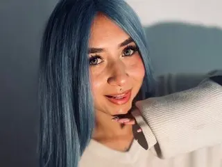 Kimeko poses with a close-up headshot, showing her long blue hair and a slight smile against a plain background.