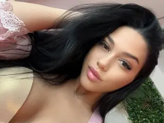 KimmBlaze poses with long black hair and pink lace lingerie, showing her cleavage and face in a close-up shot.