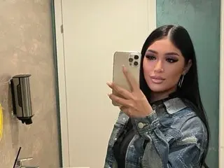 Stylish woman in a denim jacket taking a mirror selfie in a modern bathroom.