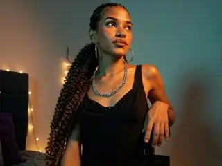 KittyLoveKm poses with her long, curly hair down, wearing a black tank top against a dark background.