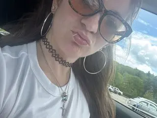 Kkrazyy67 poses in a white t-shirt with her long brown hair down, looking at the camera while outdoors.
