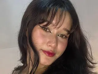 Young woman with dark bangs and red lipstick posing with a soft, moody expression indoors.