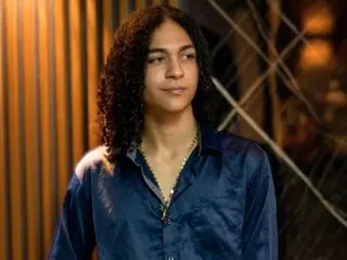 KylePresly wears a dark blue button-down shirt while looking toward the camera against a warm, dim background.