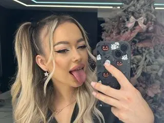 Blonde woman with star earrings taking a playful selfie in front of a decorated Christmas tree.