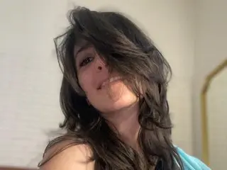 LEONAAx with long dark hair, posing close-up and smiling while looking at the camera.