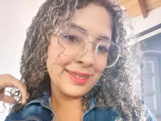 LITTLEJULES — LITTLEJULES smiles at the camera with her curly grey hair and clear glasses, wearing a blue denim shirt.
