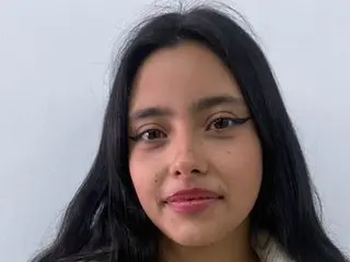 Young woman with long black hair and winged eyeliner smiling against a plain white background.