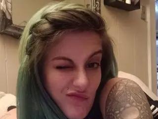 Lacifer winks at the camera, showing her face and light green hair while posing close up.