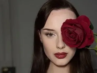 LadyHennieFaye poses with a large red rose held against her face, showing her long dark hair and red lipstick.