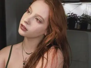 LadySlan, a redheaded woman, looks at the camera while wearing a dark green top in a close-up shot.