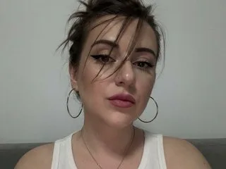 LadyVibe22 looks directly at the camera with a neutral expression, wearing a white tank top and silver hoop earrings.
