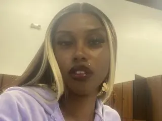 Lailani_Diore poses close-up, showing her face, blonde-streaked hair, and a nose ring while wearing a light purple top.