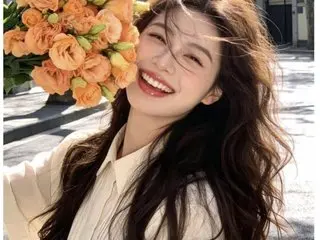 Smiling young woman in a white blouse holding a bouquet of orange roses in bright sunlight.