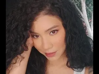 LauraEvanns poses with her hand near her face, showing her long, dark curly hair and a close-up view of her face.