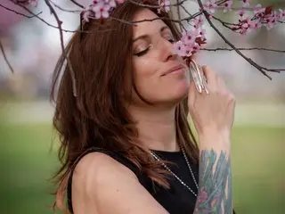 LauraHorn poses with her eyes closed, resting her chin on her hand and showing her long brown hair and black tank top against a soft outdoor background.