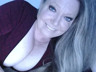 LauraLusts poses with her long blonde hair down, showing off her cleavage in a dark red top.