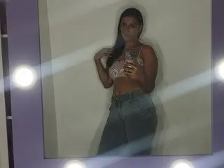 Young woman in a lace crop top and denim jeans taking a mirror selfie in a dimly lit room.
